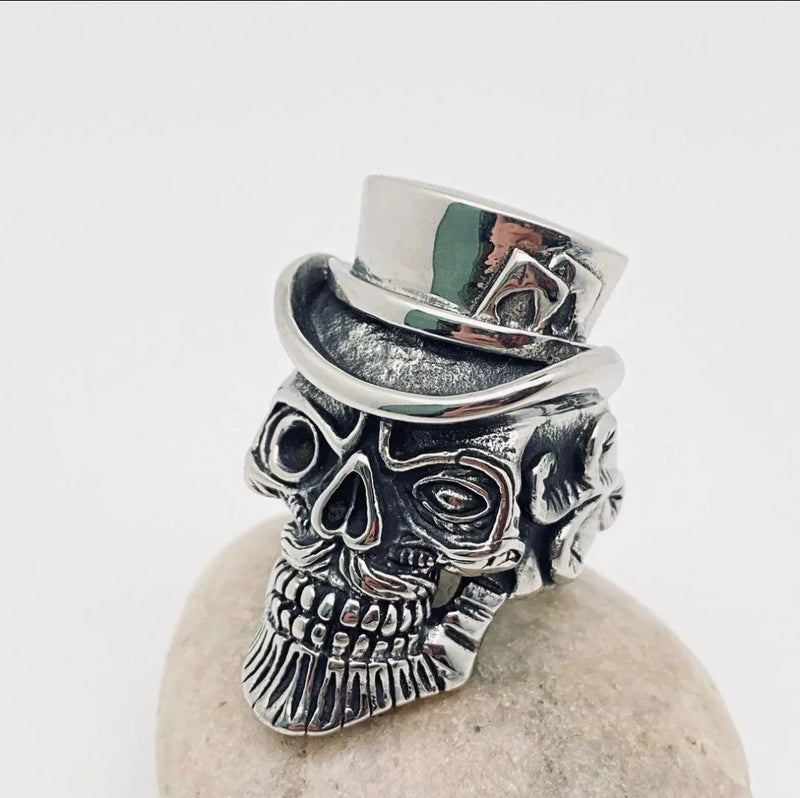 Stainless steel skull ring with top hat and detailed engraving, displayed on a stone