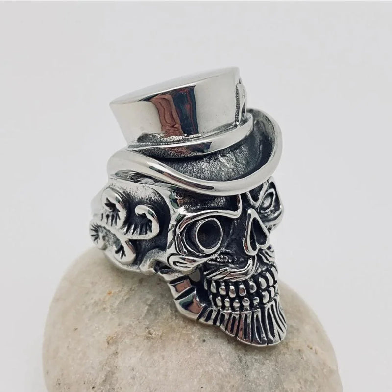 Stainless steel skull ring with top hat and ornate detailing on white stone background