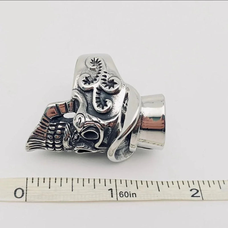 Stainless steel skull ring with intricate engraved details beside a measuring tape