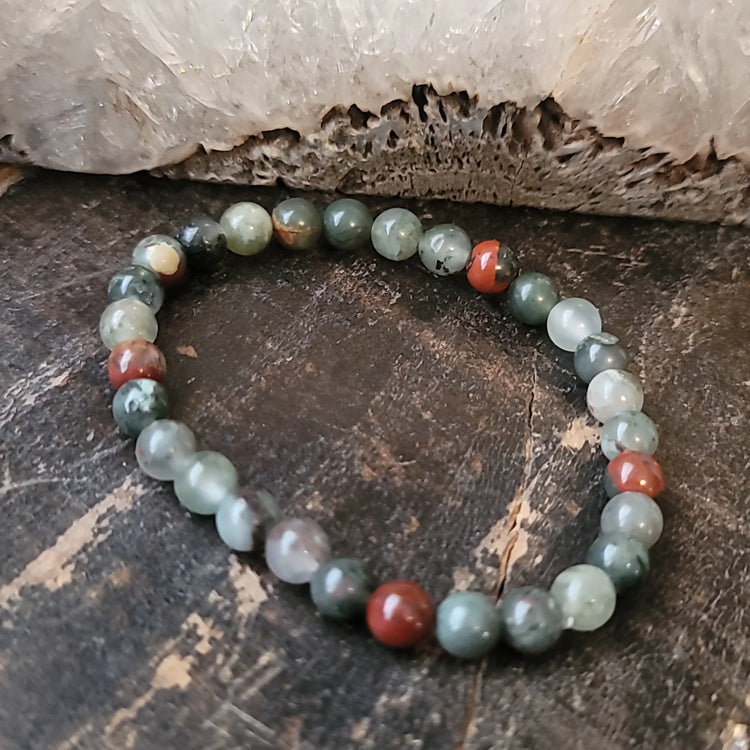 Moss agate and jasper crystal bead bracelet on rustic wood near a clear quartz cluster