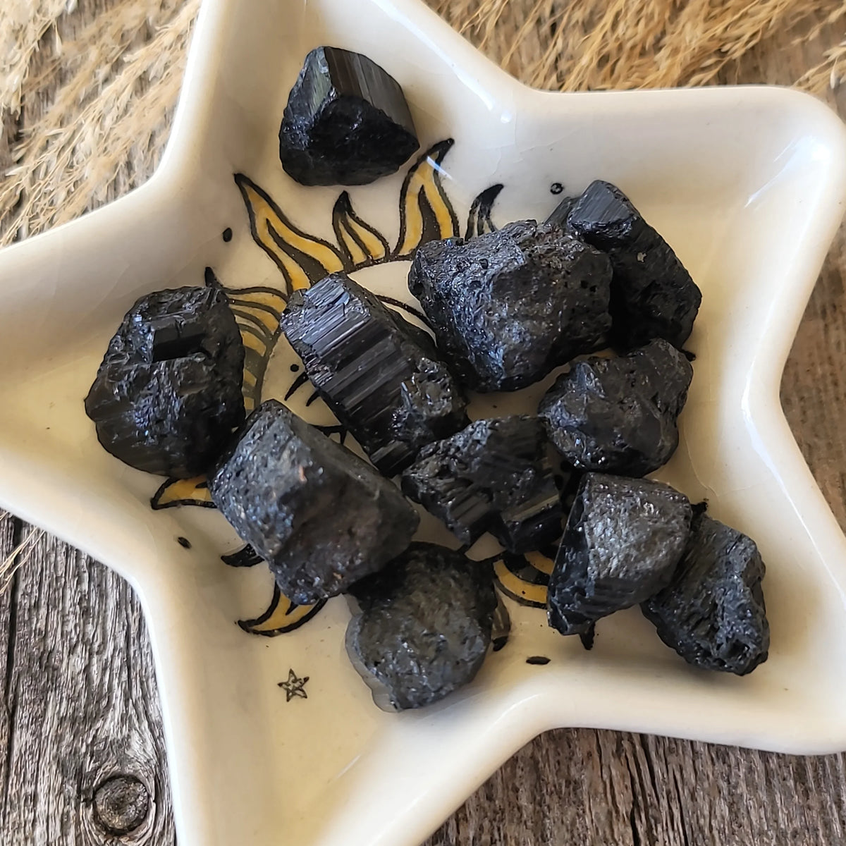 Raw black tourmaline crystals in a star-shaped dish on a rustic wooden surface