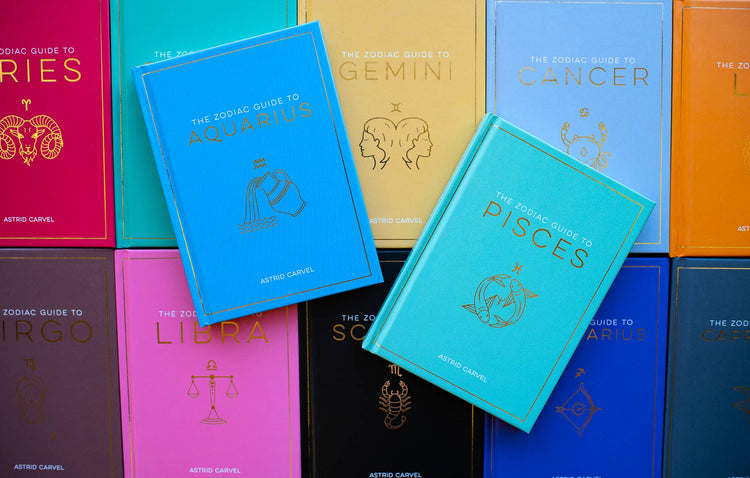 Colorful astrology books featuring zodiac guides for Aquarius and Pisces on display