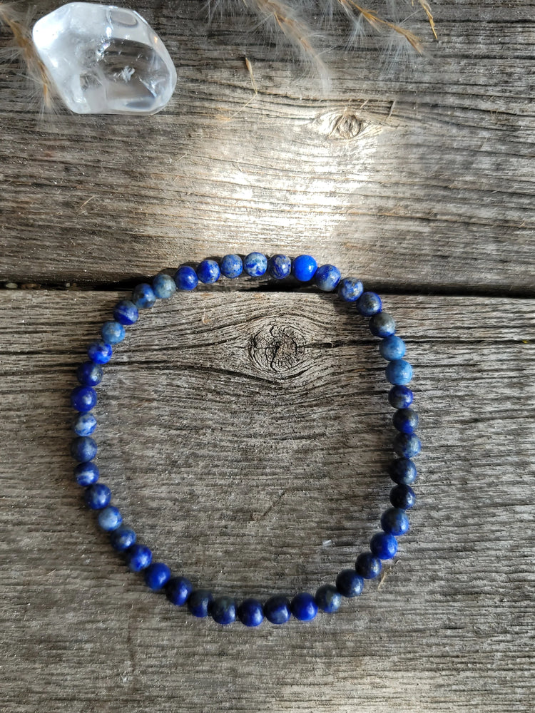 Lapis lazuli beaded bracelet on rustic wood with clear quartz crystal nearby