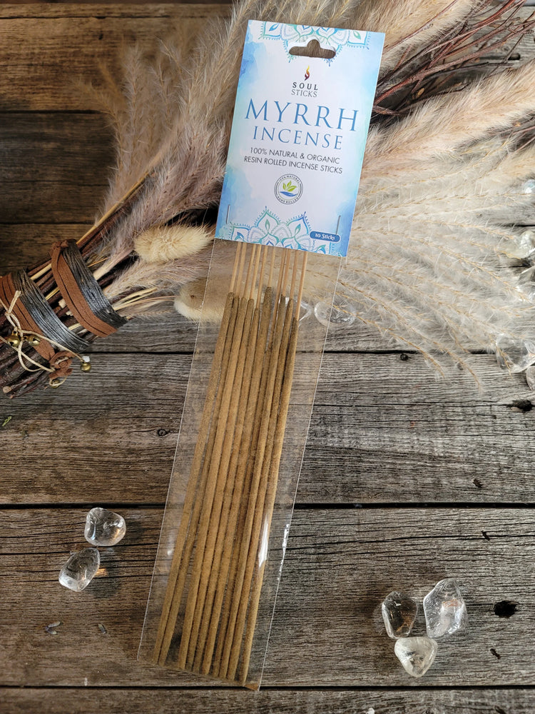 Myrrh incense sticks in clear packaging on rustic wood with crystals and dried grass