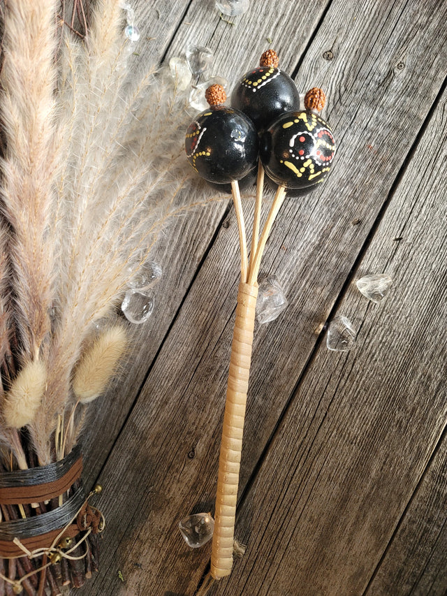 Decorative hand-painted black rattle with seed pods, crystals, and dried grasses on wood.