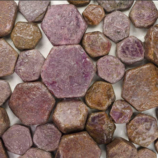 Raw hexagonal ruby crystals in shades of purple and brown, arranged on a flat surface