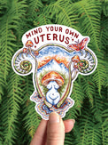Mind Your Own Uterus vinyl sticker, a uterus shaped landscape with mushrooms and a goddess figure
