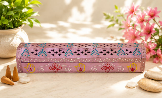 Hand-painted pink incense burner with Hamsa hands, floral motifs, and incense cones, surrounded by stones and greenery for spiritual ambiance