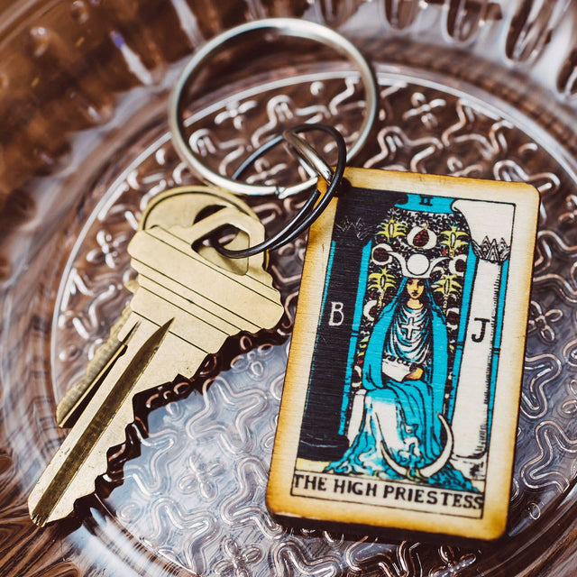 Wooden High Priestess tarot keychain with brass key on ornate glass tray, metaphysical decor