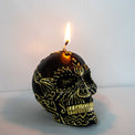 Black skull candle with gold decorative patterns burning on a light background