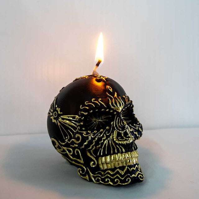 Black skull candle with gold decorative patterns burning on a light background