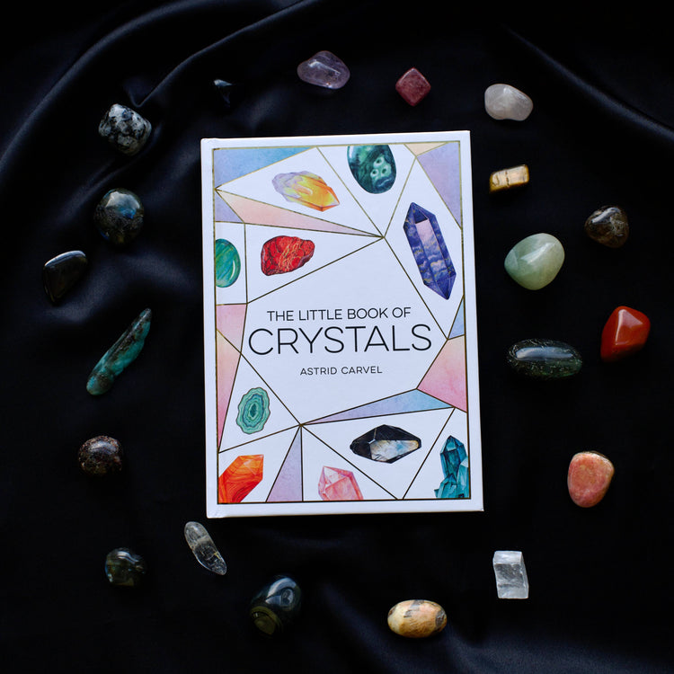 The Little Book of Crystals by Astrid Carvel surrounded by assorted healing crystals on black fabric