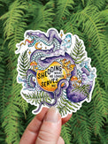 Shedding Snake vinyl sticker, a snake coiled around a glowing circle, held against ferns