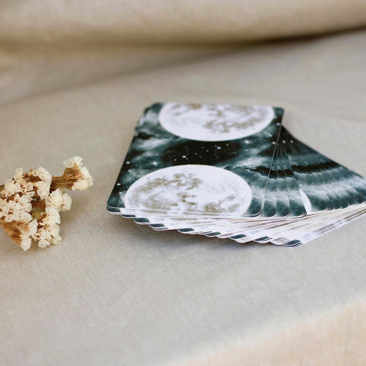 Moon phase tarot cards with celestial design, beside dried flowers on linen
