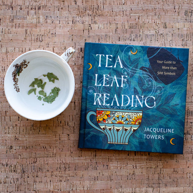 Tea leaf reading guide book with tea leaves in cup on cork surface, spiritual divination tool