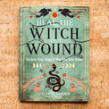 Heal the Witch Wound book by Celeste Larsen with snake, moon phases, and floral design on cork background