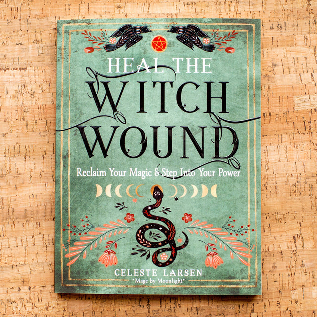 Heal the Witch Wound book by Celeste Larsen with snake, moon phases, and floral design on cork background