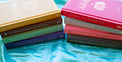 Colorful stack of astrology zodiac guidebooks for Gemini, Virgo, Pisces, Sagittarius, Aries, Cancer, Libra, and Capricorn on blue fabric.