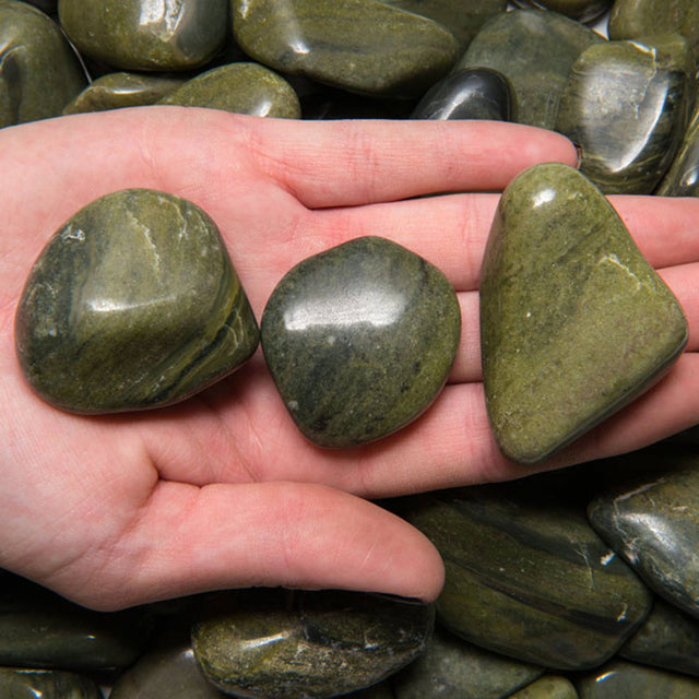 Hand holding three polished green serpentine stones, used for crystal healing and meditation