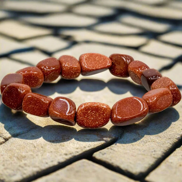 Polished goldstone crystal bracelet with brown glittery beads on stone background