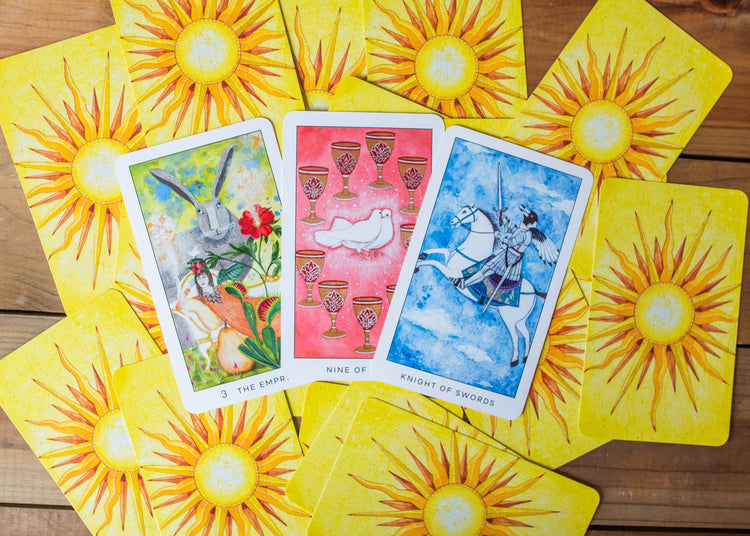 Colorful tarot cards including Empress, Nine of Cups, and Knight of Swords on wooden table