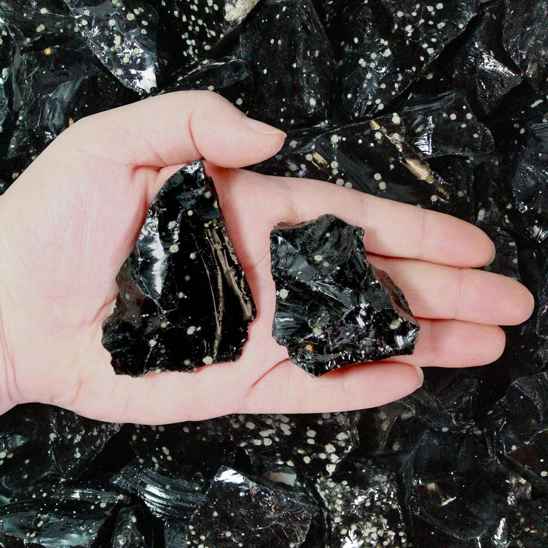 Hand holding two snowflake obsidian crystals with black and white speckled pattern