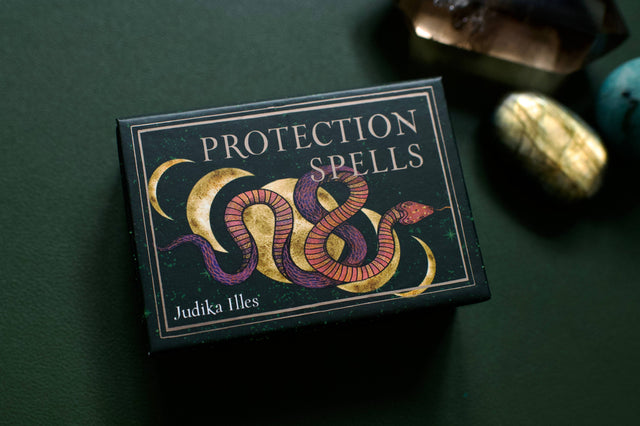 Protection Spells card deck box with crescent moons and snake illustration, crystals nearby