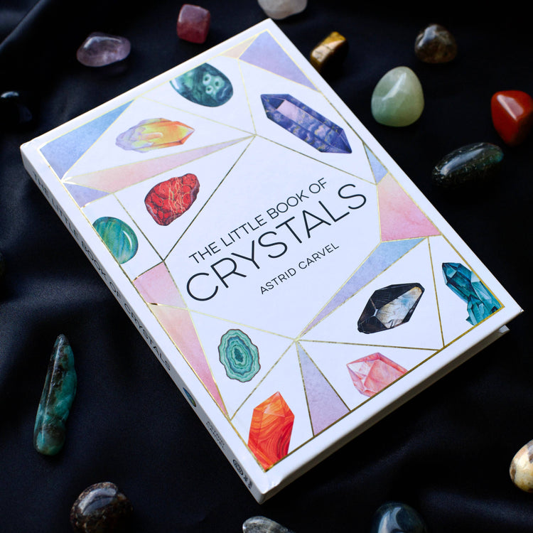 The Little Book of Crystals by Astrid Carvel surrounded by colorful crystals on black fabric.