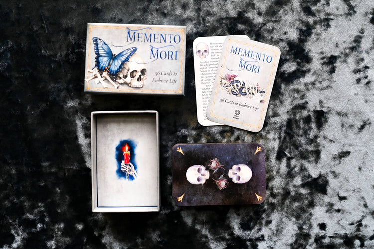 Memento Mori oracle card deck with skull, butterfly, and candle artwork on textured surface