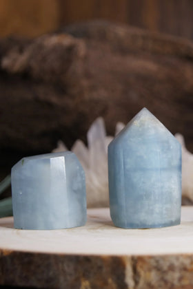 Two polished blue aquamarine crystal towers on a wooden surface with blurred background