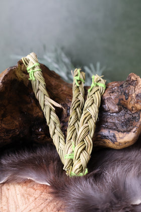 Three DESIGNS BY DEEKAY INC sweet grass braids tied with green string on a wooden log and fur background.