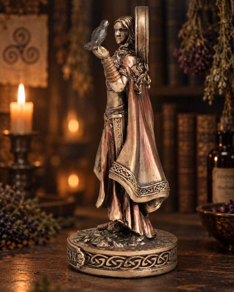 A detailed gothic figurine of a woman holding a raven, standing on a circular base with Celtic knot patterns. The figurine has a weathered metallic finish with bronze, silver, and dark brown tones, set against a dark, atmospheric background with a lit candle and books.