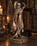 A fantasy warrior figurine with a bird on her raised hand, standing on a decorative base in a warmly lit, rustic room with bookshelves and candles in the background.