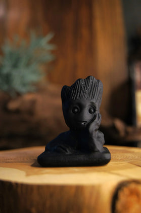Hand-carved black obsidian Groot figure on wood with blurred natural background