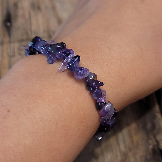 Amethyst chip bracelet on wrist, natural purple stones, wooden background
