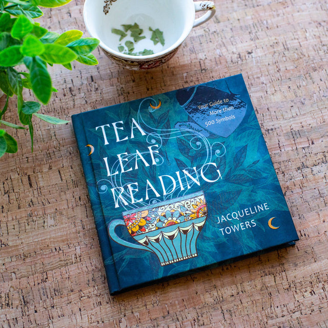 Tea Leaf Reading book by Jacqueline Towers with teacup and leaves on cork surface, metaphysical guide