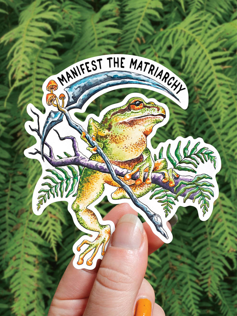 Manifest the Matriarchy vinyl sticker, a tree frog holding a scythe on a mushroom covered branch