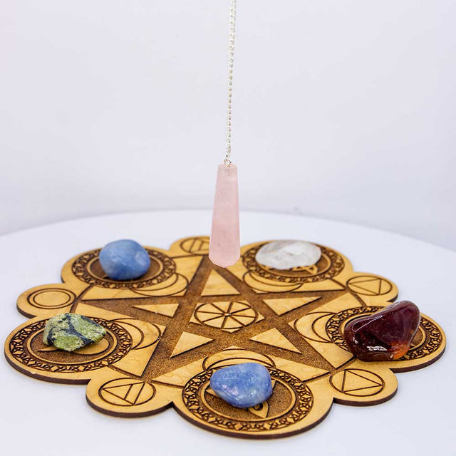 Rose quartz pendulum over wooden chakra grid with healing crystals for spiritual balance and energy work