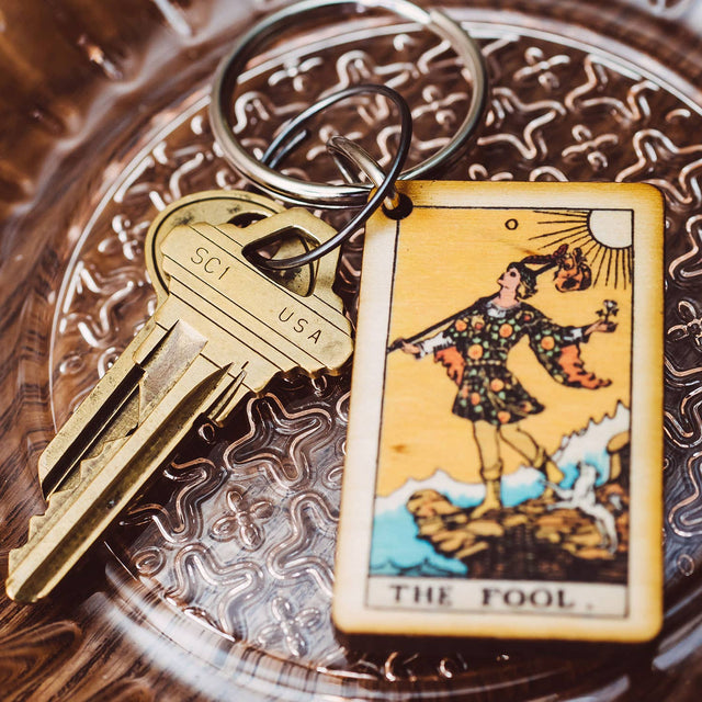 The Fool tarot card keychain on ornate glass dish with brass keys, spiritual decor