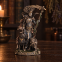 A detailed fantasy figurine of a horned female warrior holding a scythe, standing on a base labeled 'HELL' with a dark dog at her side, photographed on a wooden surface with a blurred candlelit background.