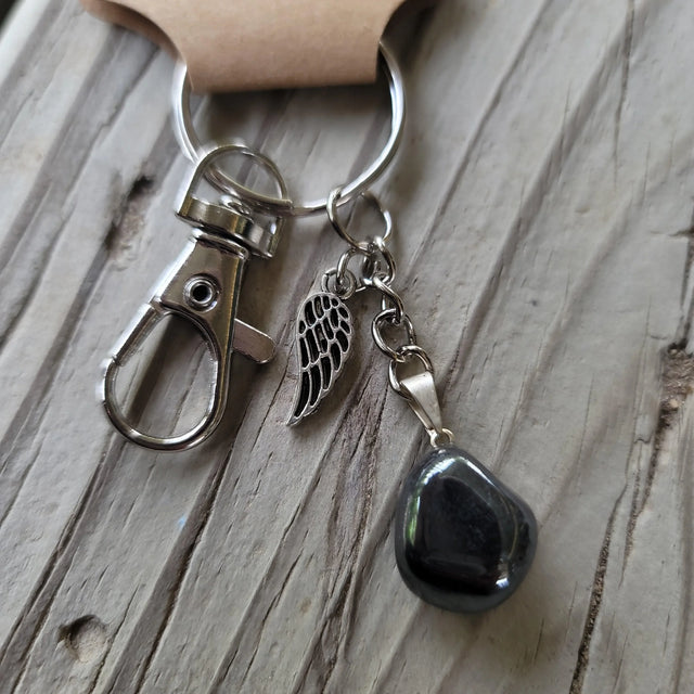 Hematite crystal keychain with silver wing charm on rustic wood surface