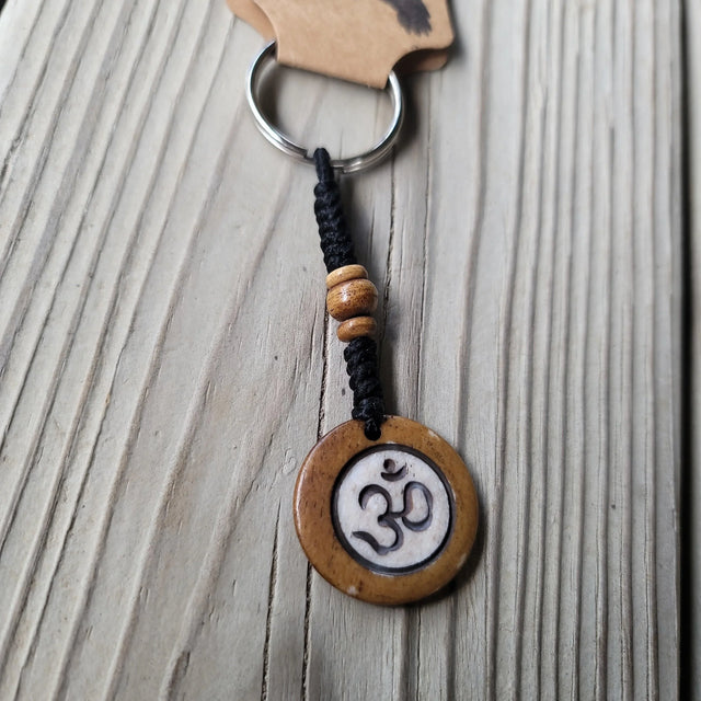 Wooden Om symbol keychain with black macrame cord and bead on rustic wood background