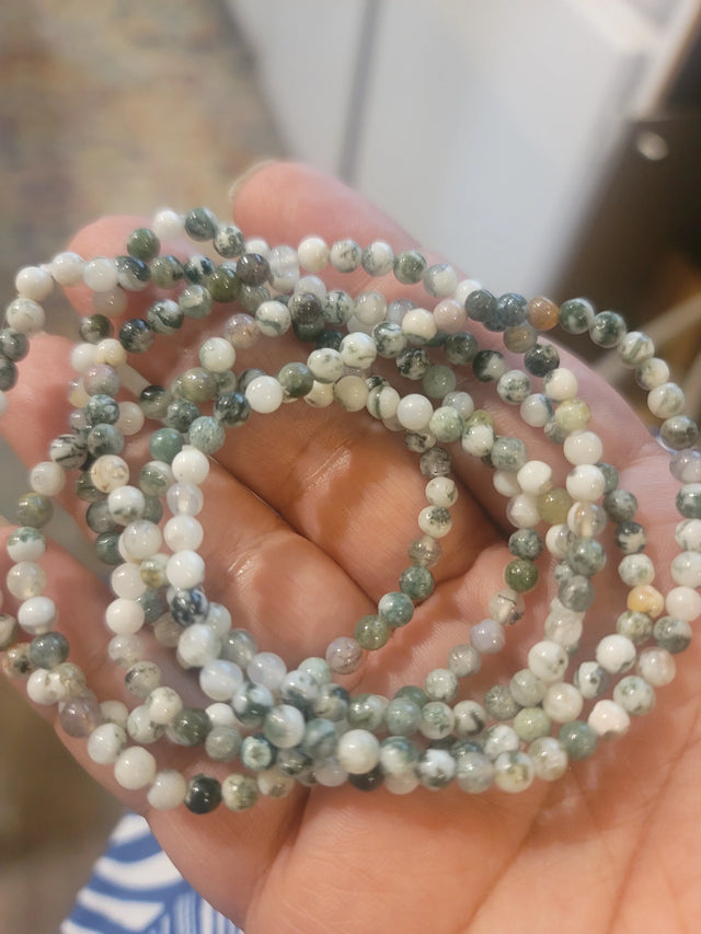 Hand holding green and white crystal bead bracelets, metaphysical jewelry for healing